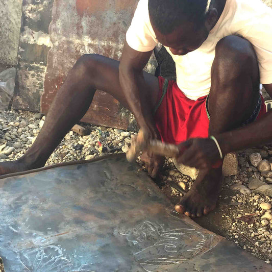 Haitian artisan creating wall art from recycled 55-gallon metal oil drums.