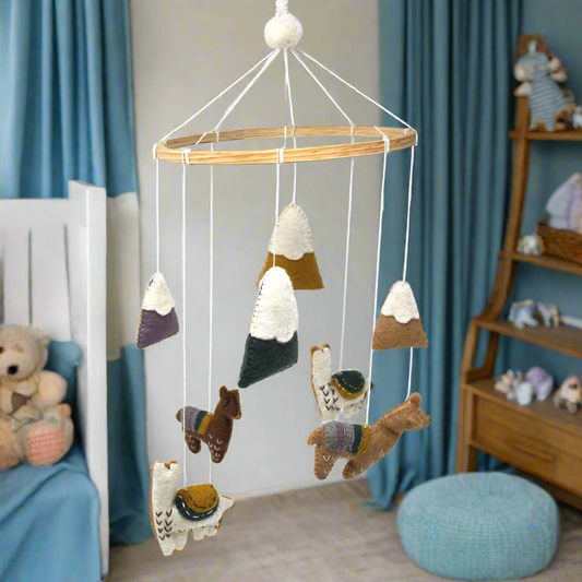 boys room in blue with hand-felted baby mobile hanging from a bamboo hoop. Mobile has four felt baby llamas and four felt snow capped mountains. fair trade product created by female artisans in Nepal and fair trade imported to the US.