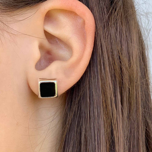 Close-up of an ear wearing a gold and black square earring.
