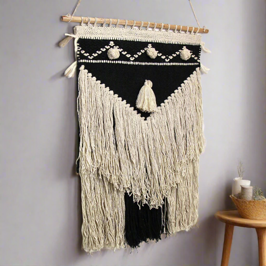 handmade macrame wall hanging in natural and dark blue along side a chair with matching natural colored macrame long pillow cover. Handmade and fair trade imported from New Delhi, India.