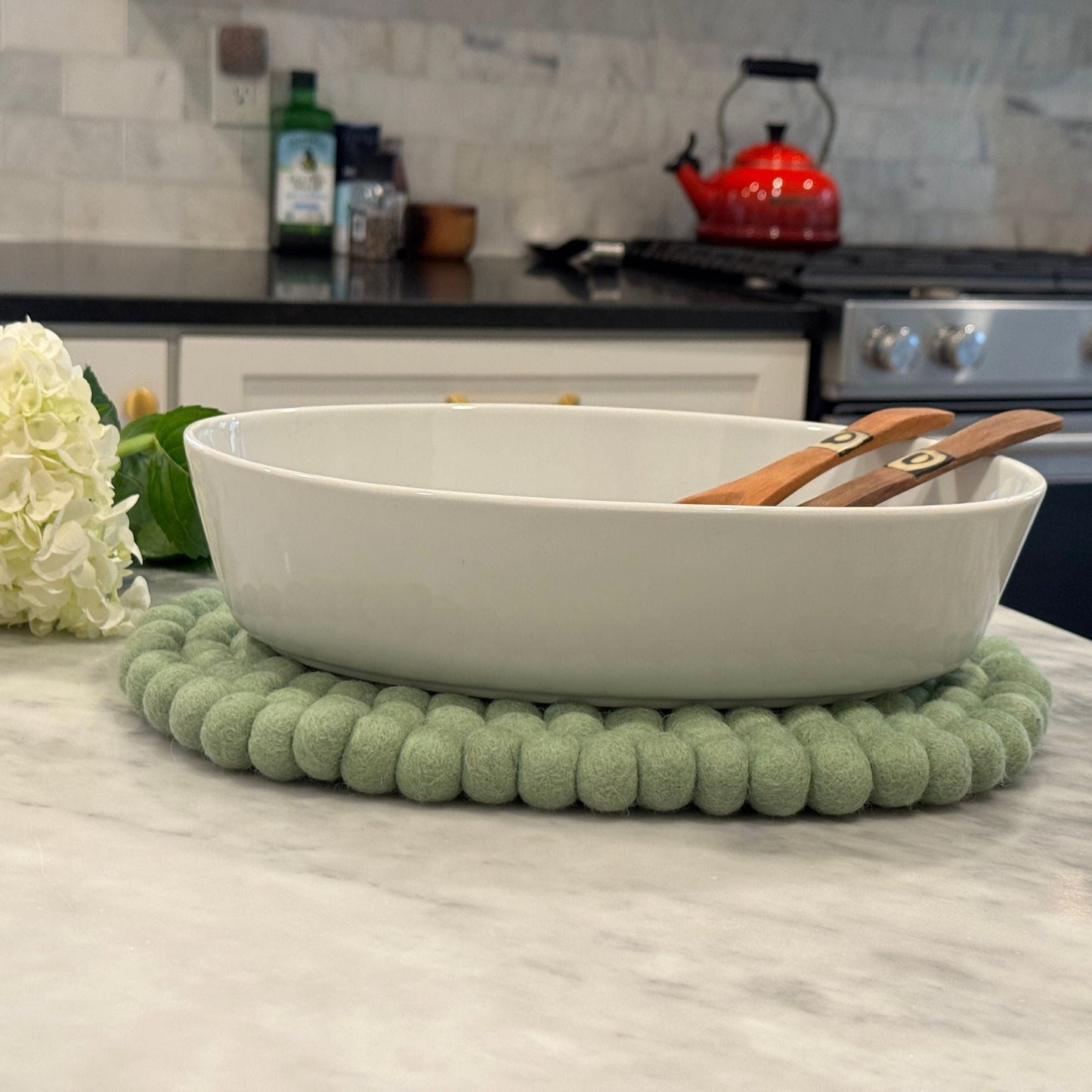 White oval dish on a light green felt ball trivet in a kitchen setting