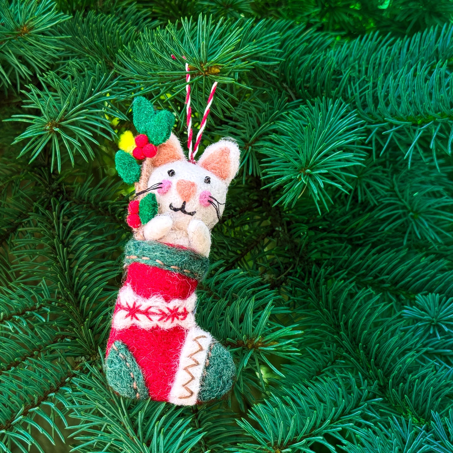 Felted cat ornament in a red and green stocking on a Christmas tree.