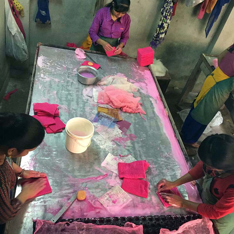 People working with pink fabric on a large table in a workshop setting.