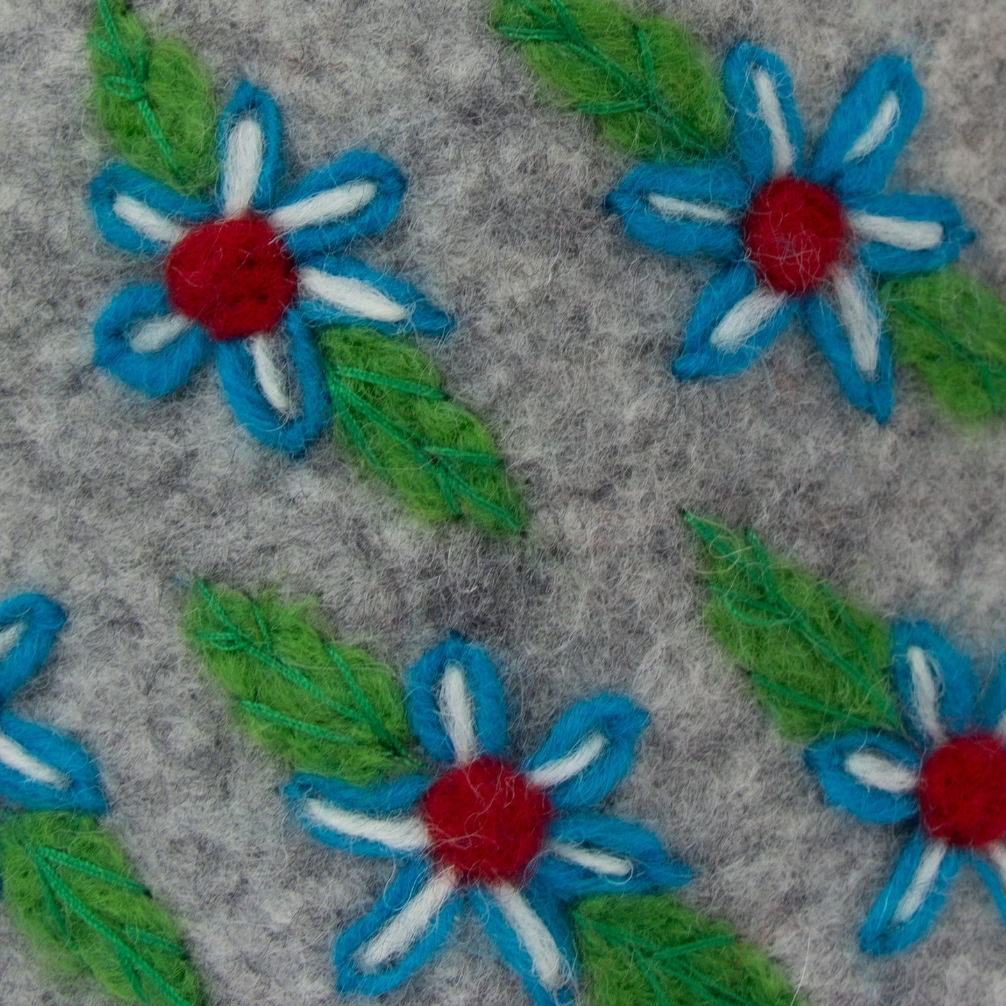 Close-up of embroidered flowers with blue petals, red centers, and green leaves on a gray fabric background.