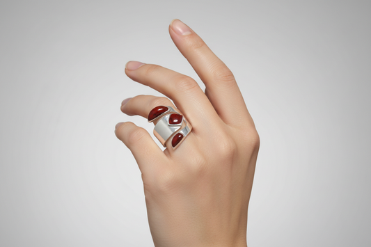 Hand wearing a silver ring with red Jasper stones on a light gray background