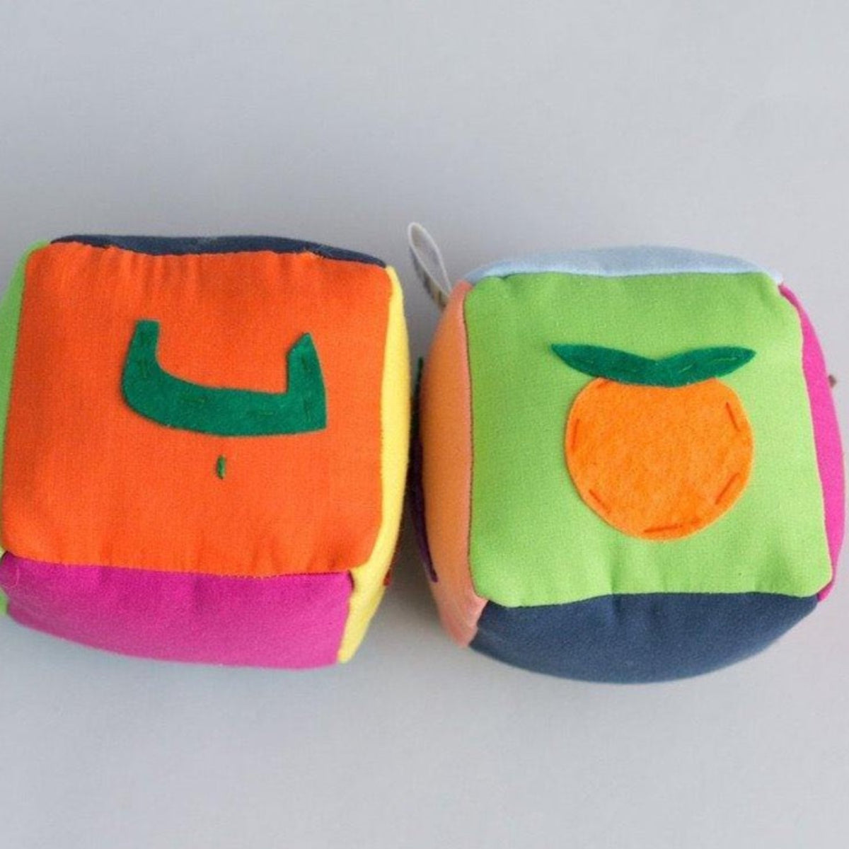Two colorful fabric blocks with fruit designs and stitched Arabic letters on a white background.