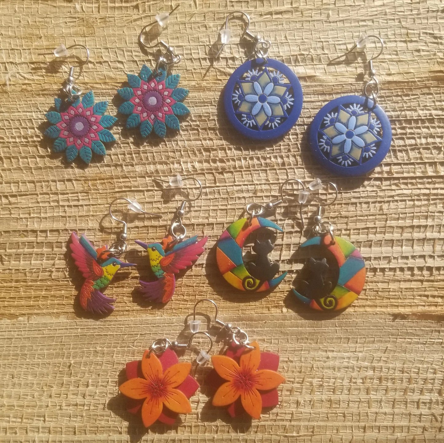 Colorful carved gourd floral, hummingbird, and cat on the moon earrings on a woven surface