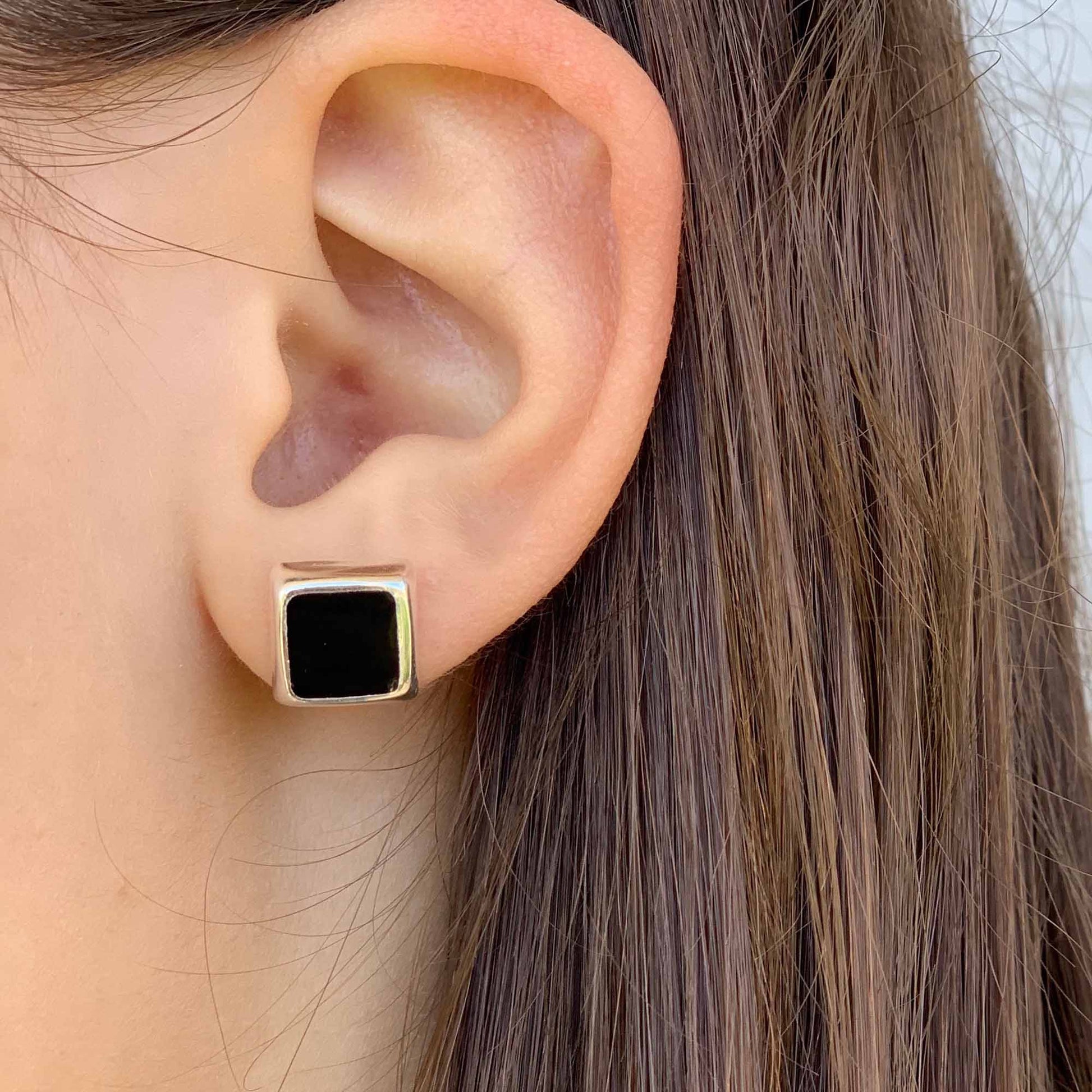 Close-up of an ear wearing a gold and black square earring.