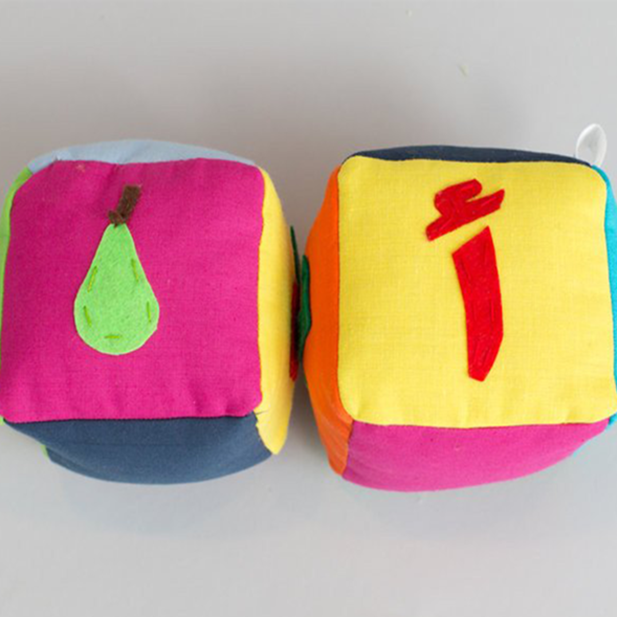 Two plush blocks with Arabic letters and fruit images on them, designed for educational purposes.