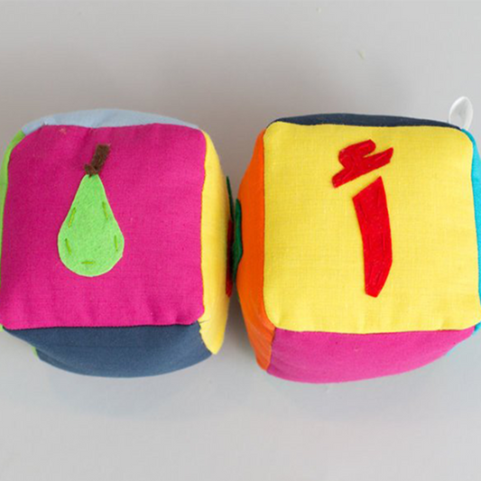 Two plush blocks with Arabic letters and fruit images on them, designed for educational purposes.