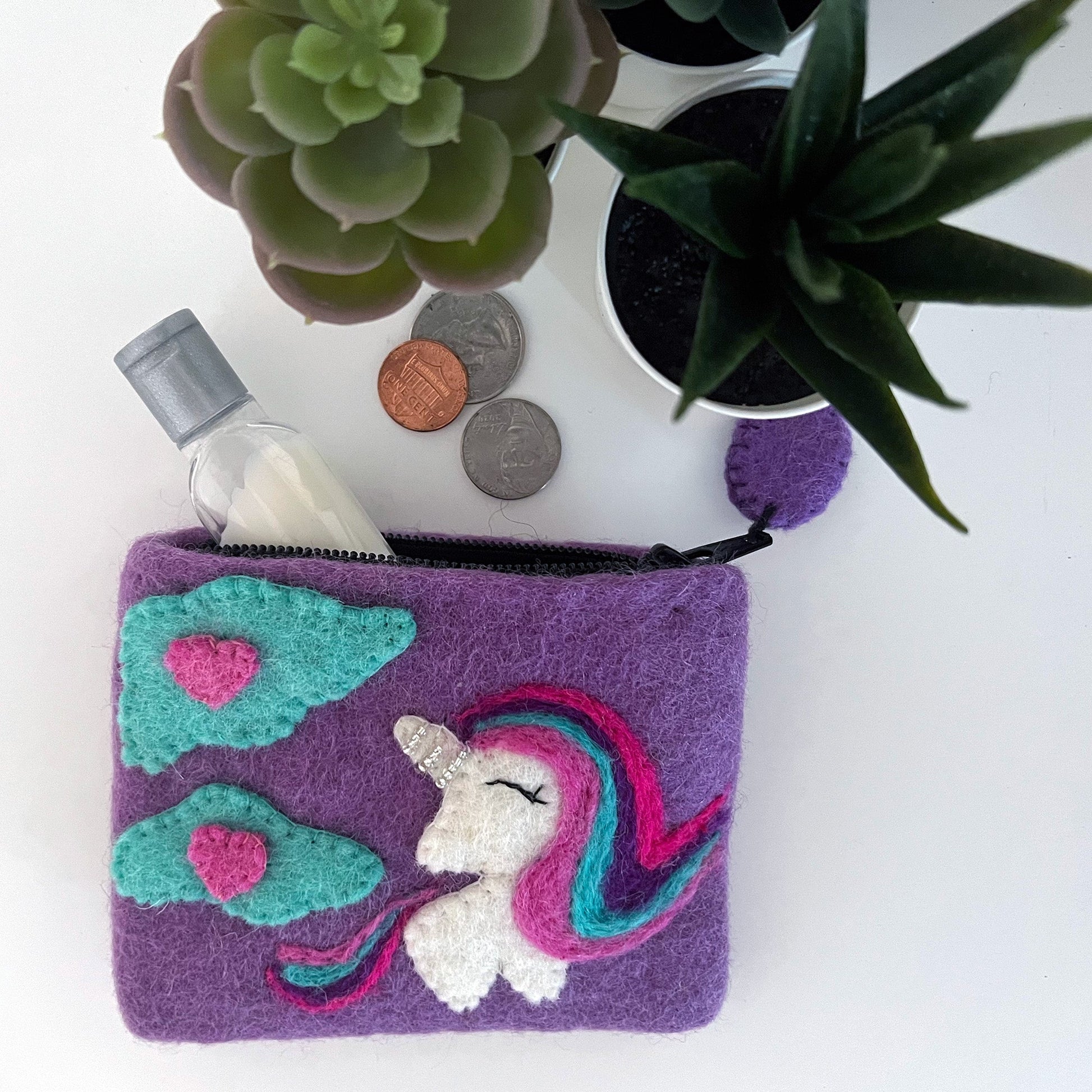 Purple coin purse with unicorn design on a white surface with plants and coins.