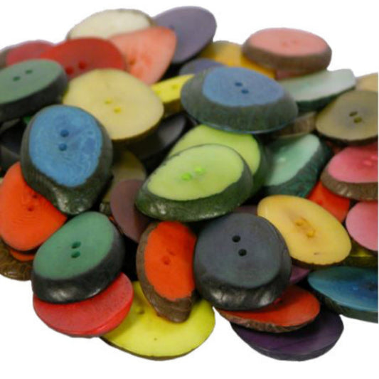 A pile of colorful oval tagua slice buttons with two holes, shown in a variety of colors including blue, green, yellow, orange, pink, purple, and brown on a white background.